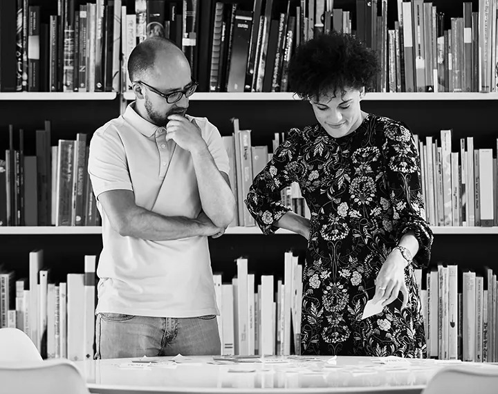A man and woman standing in front of a bookshelf, looking at books together.