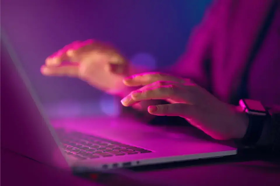 A person typing on a laptop computer in a dimly lit room